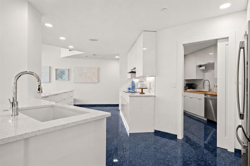 The main kitchen looking through an open doorway to the concealed prep kitchen beyond, with butcher-block counters and a stainless refrigerator visible through the opening