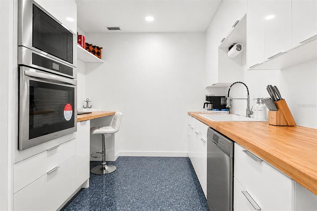 The concealed prep kitchen with butcher-block counters, a wall oven and microwave, a dishwasher, a knife block, and a small built-in desk nook with a stool