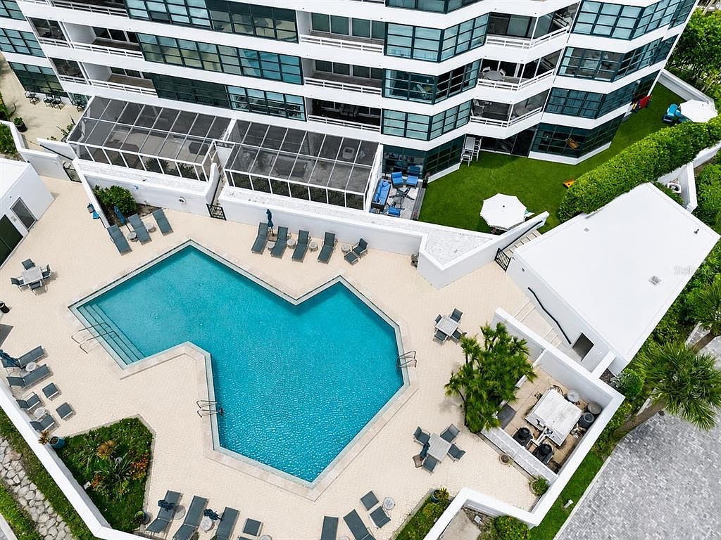 Aerial view of the community resort pool with lounge chairs and umbrellas beside the waterfront condominium building